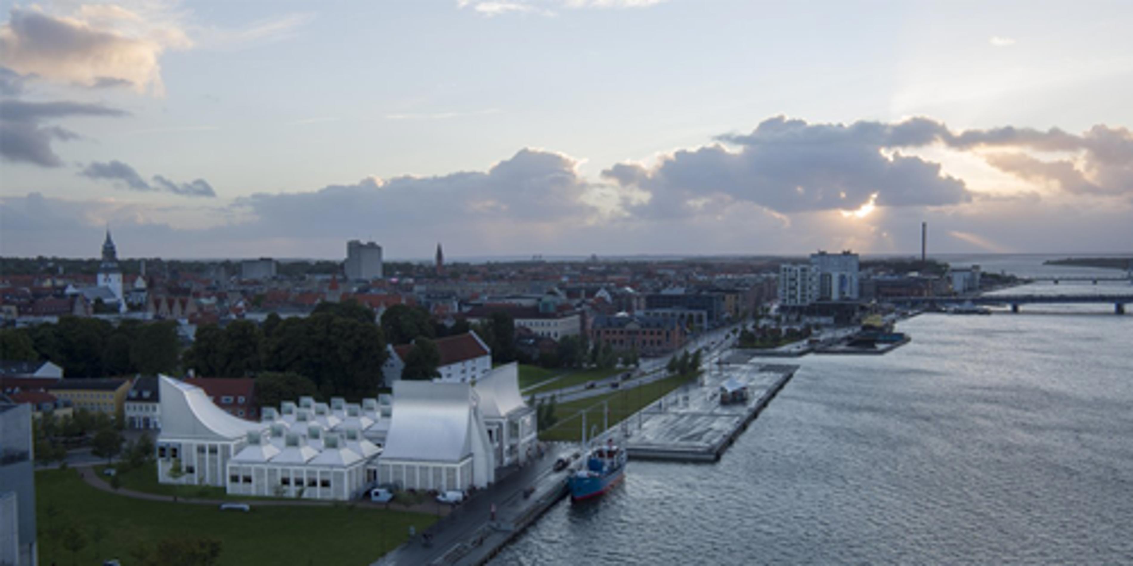 Kulturbygningen Musikkens Hus ved Aalborg havnefront med byens skyline og solnedgang i baggrunden.