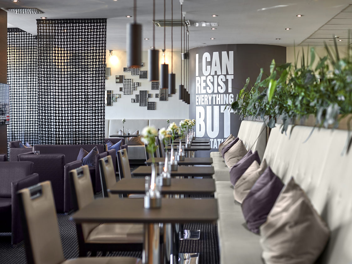 Moderne caféinteriør med polstrede stole og planter på et elegant bord, set fra sidevinkel.