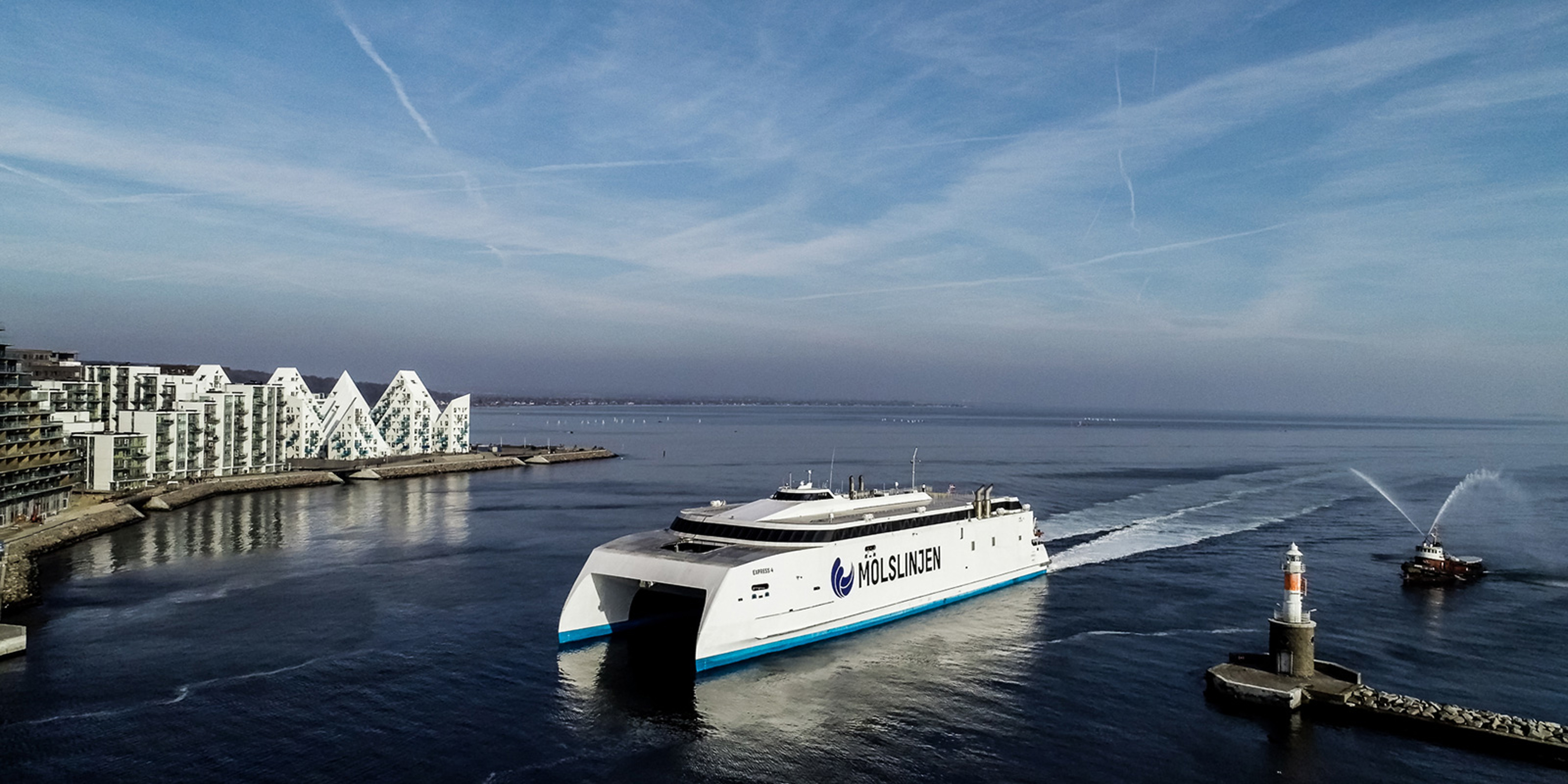 Molslinjen Express4 ferry traveling on calm sea near coastal buildings and lighthouse in the distance.