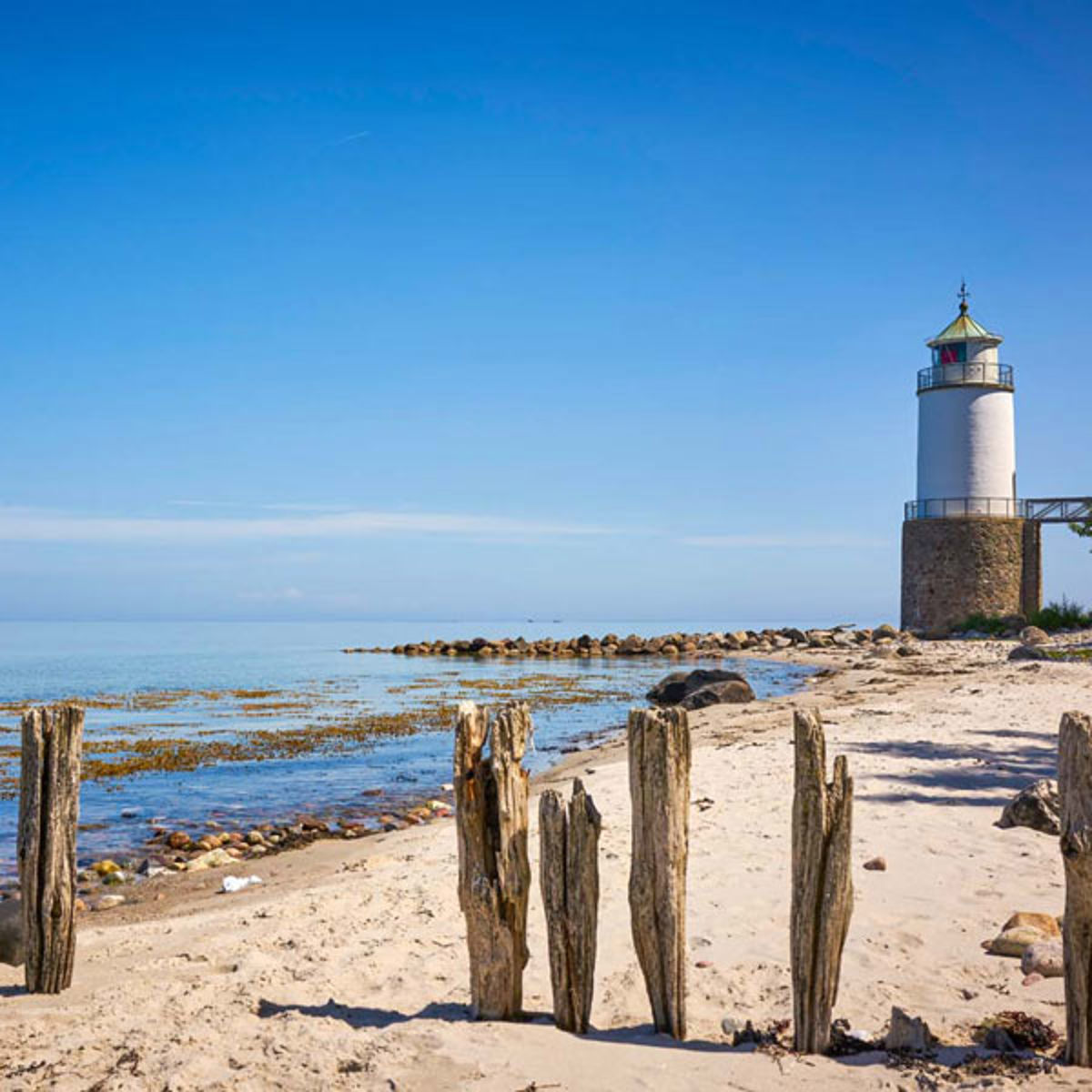 Et fyrtårn ses i baggrunden på en sandstrand på Als.