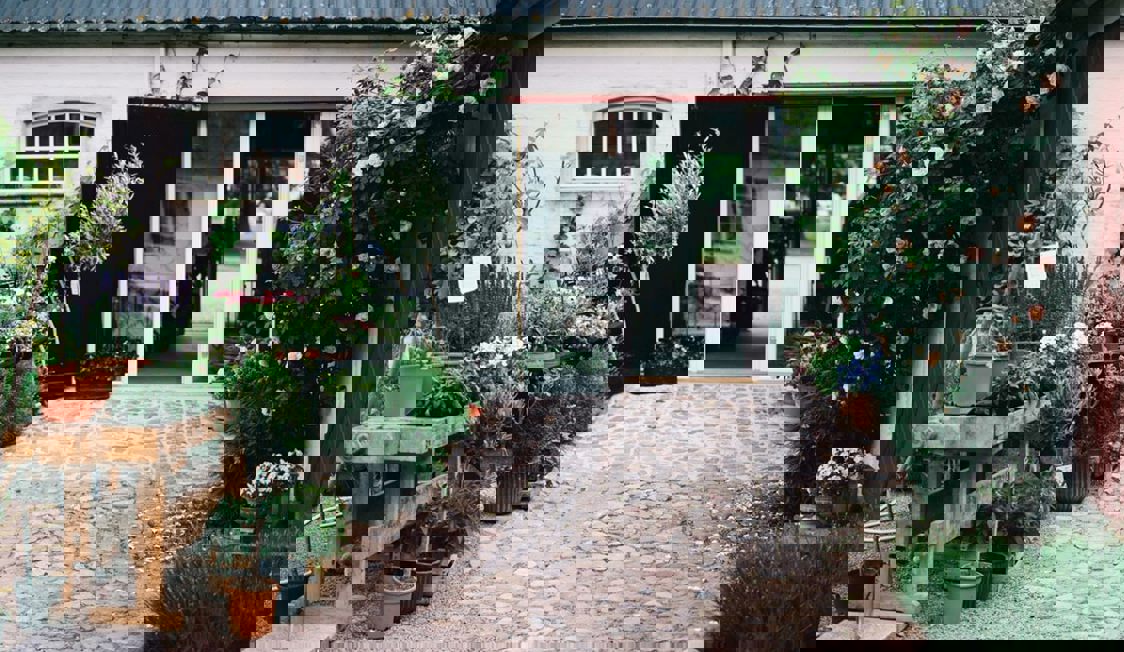 Indgangen til Hillesdal ses med brostensbelagt indgang og buske og træer