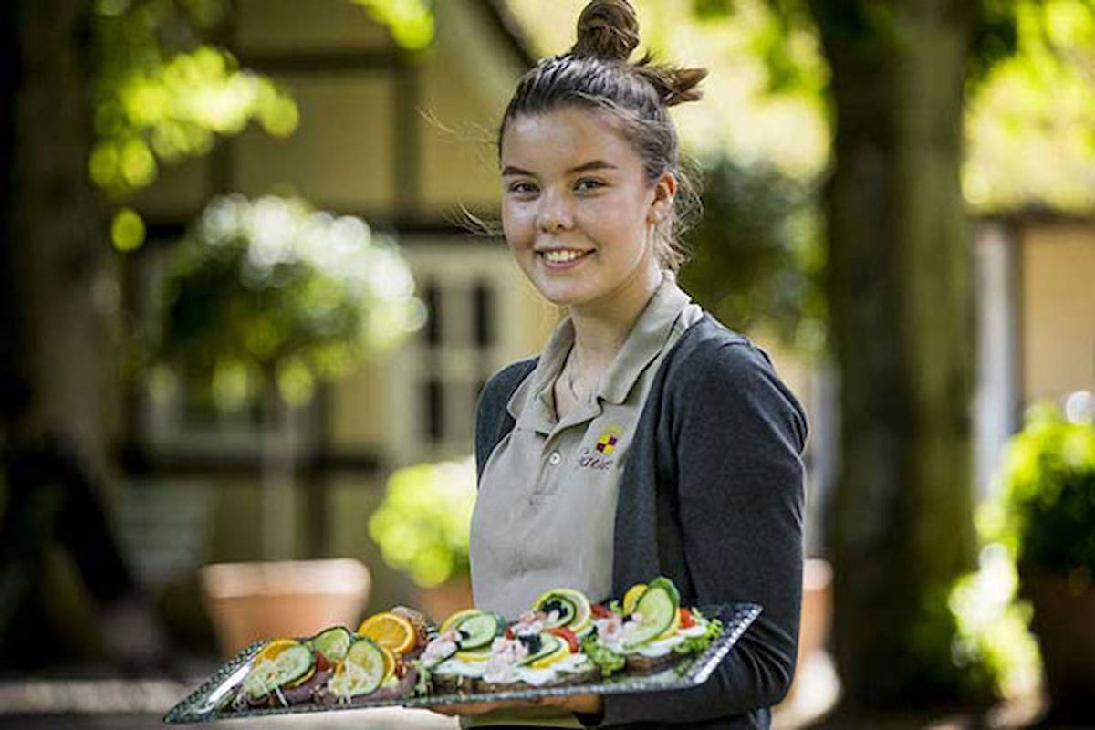 Servitrice på Ganvø Slor smiler og står med smørrebrød i hånden.
