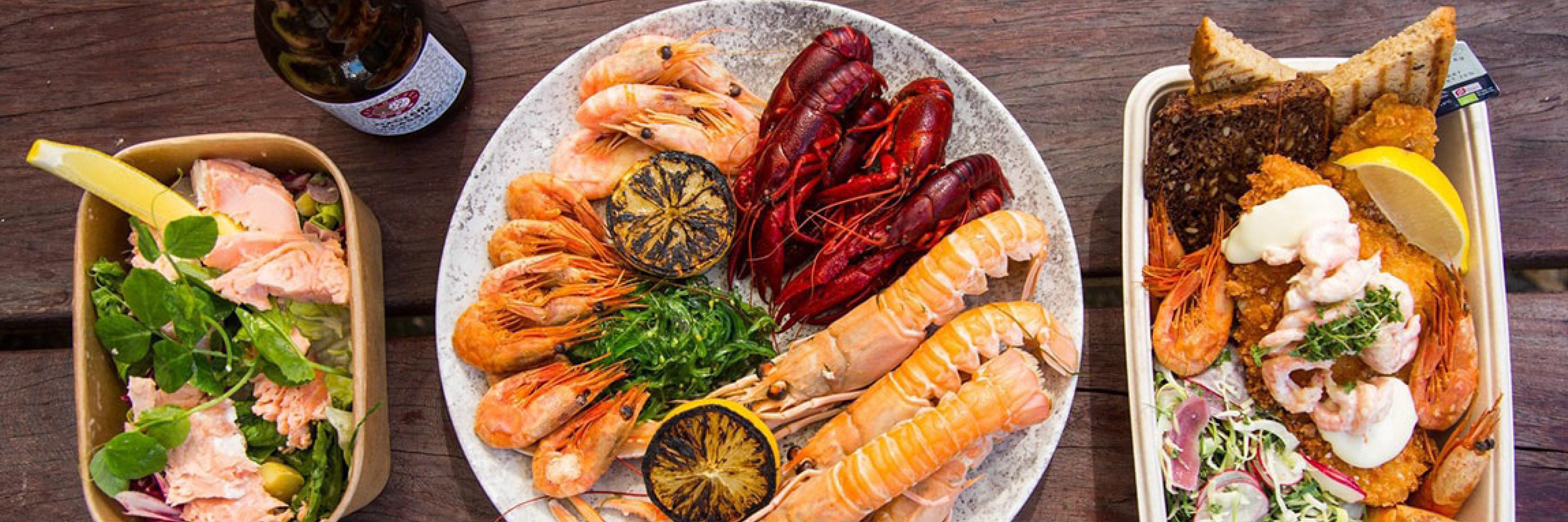 Skaldjurstallrik med räkor, kräftor och lax serverad på ett rustikt bord med citron och grönsakssallad.