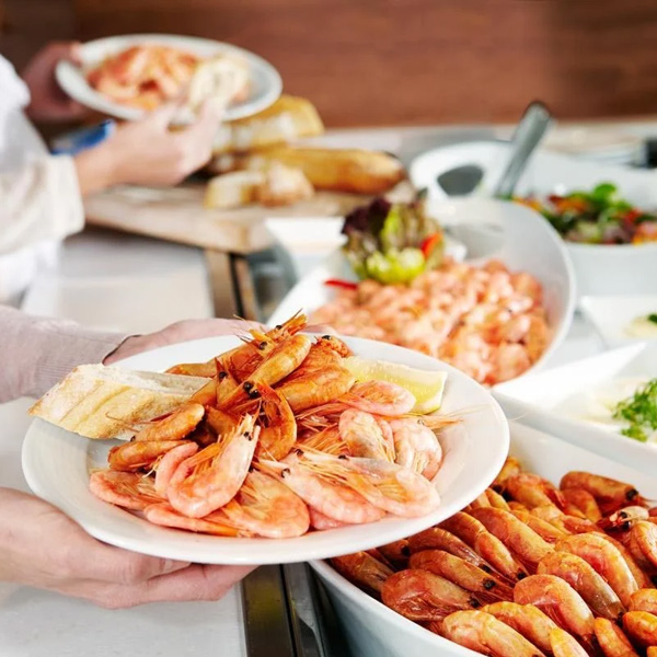 Friskkogte rejer anrettet på en tallerken med skiver af brød og citron ved en buffet i en restaurant.