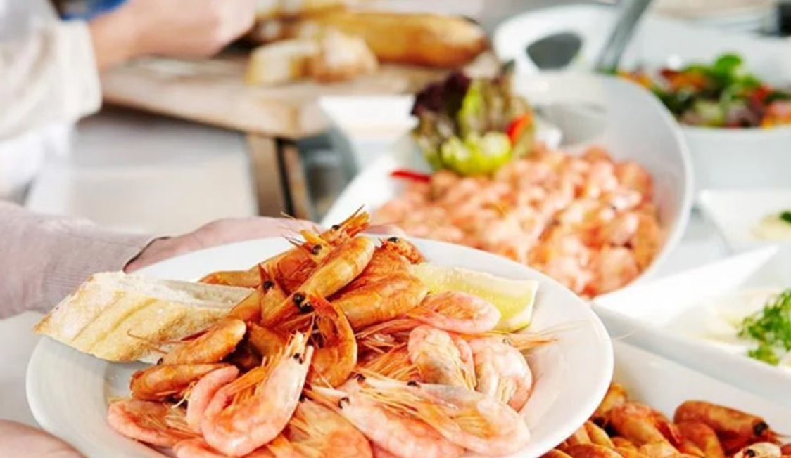 Friskkogte rejer anrettet på en tallerken med skiver af brød og citron ved en buffet i en restaurant.