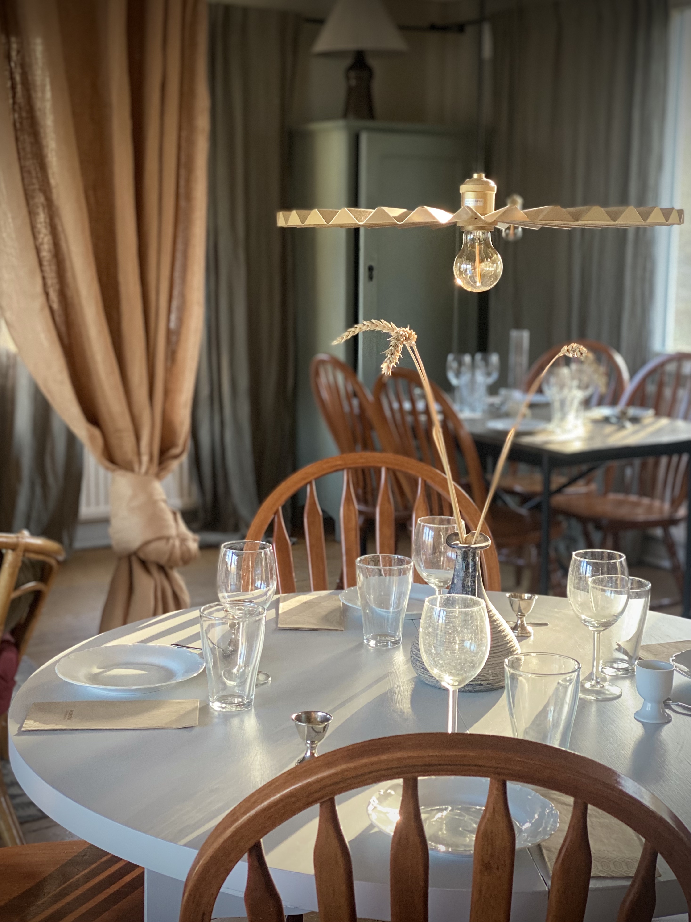 Rundt spisebord med træstole, opstillet med glas og porcelæn, under en elegant trælampe i en hyggelig spisestue.