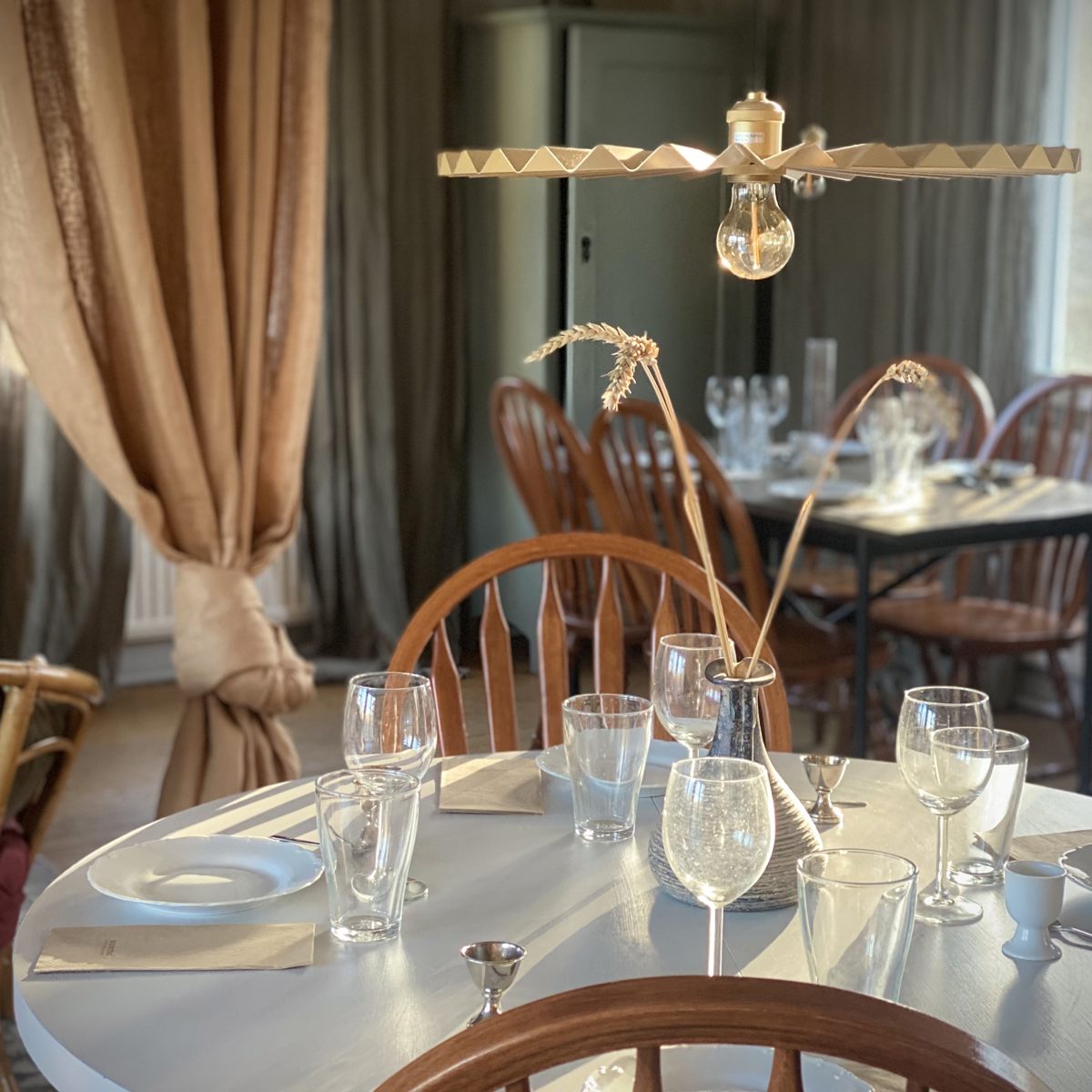 Rundt spisebord med træstole, opstillet med glas og porcelæn, under en elegant trælampe i en hyggelig spisestue.