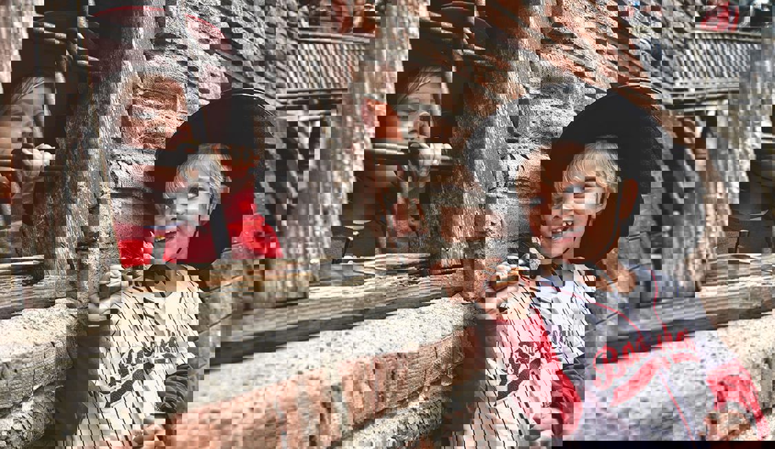 To børn står på hver deres side af et vindue med tremmer, begge iført cowboyhat.