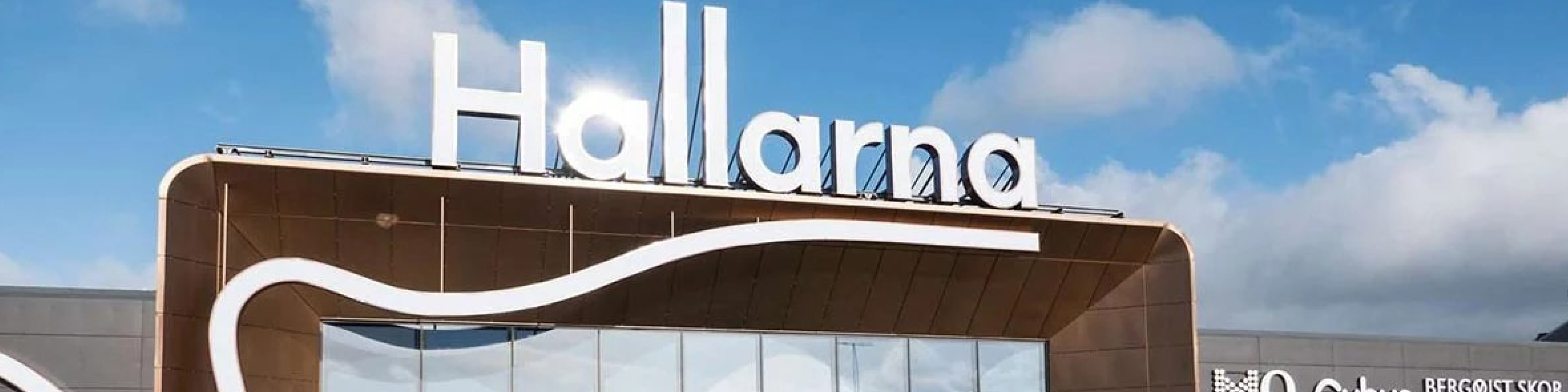 Hallarna indkøbscenter facade med moderne skiltning under en klar blå himmel med hvide skyer.