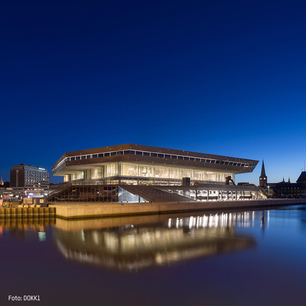 Moderne arkitektur af Dokk1 ved havnefronten i Aarhus, belyst mod en dybblå nattehimmel.