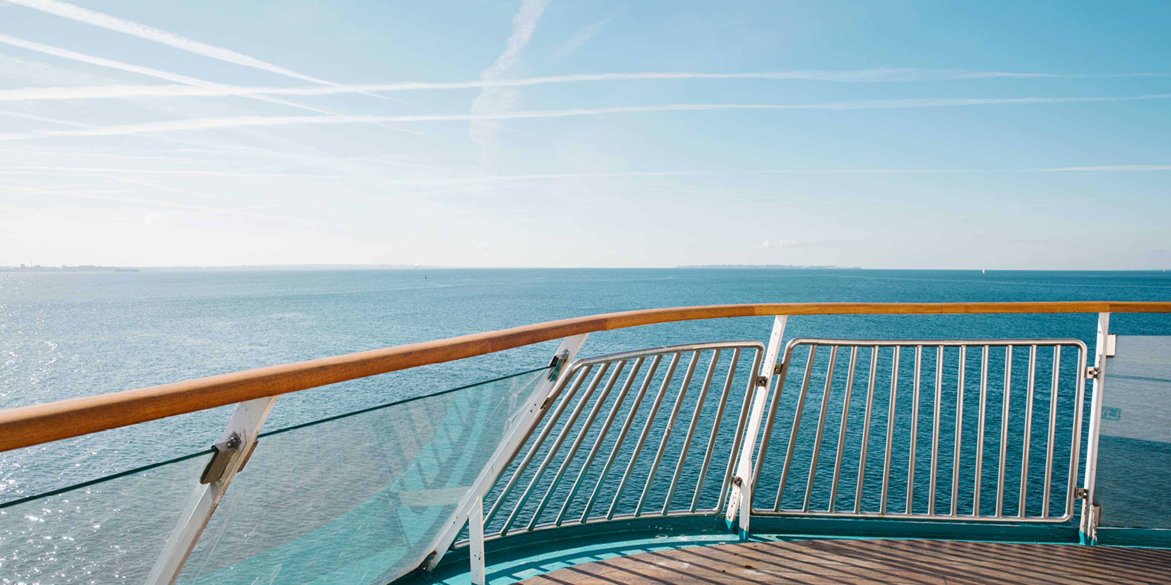 Ferry deck with wooden and metal railing overlooking the open sea beneath a clear blue sky.