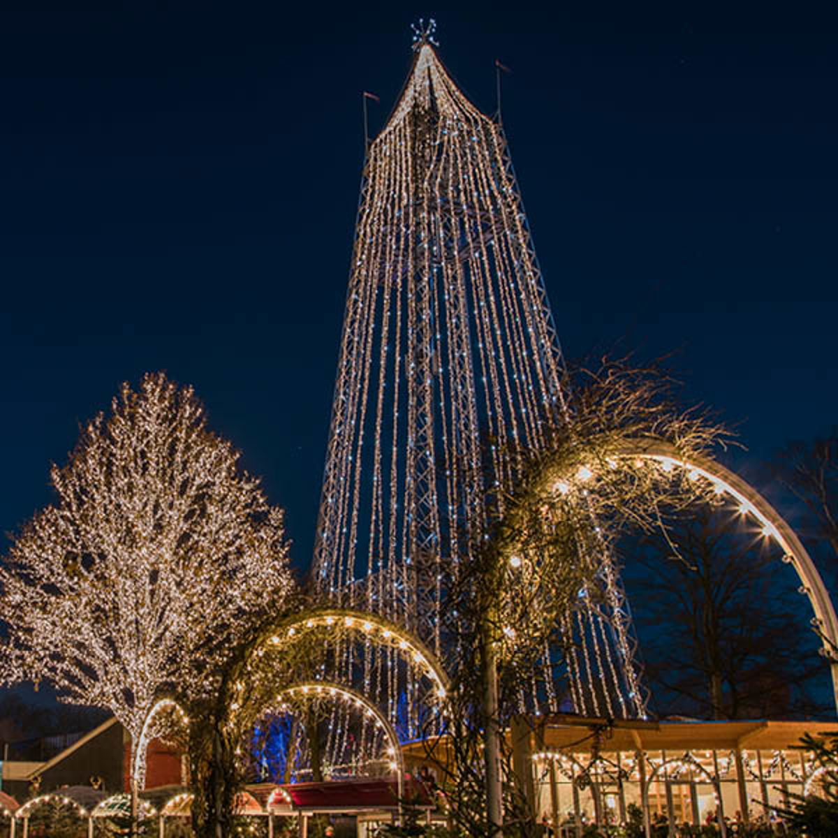 Tivoli juletræ oplyst af tusindvis af lys om natten med dekorerede lysbuer i forgrunden.