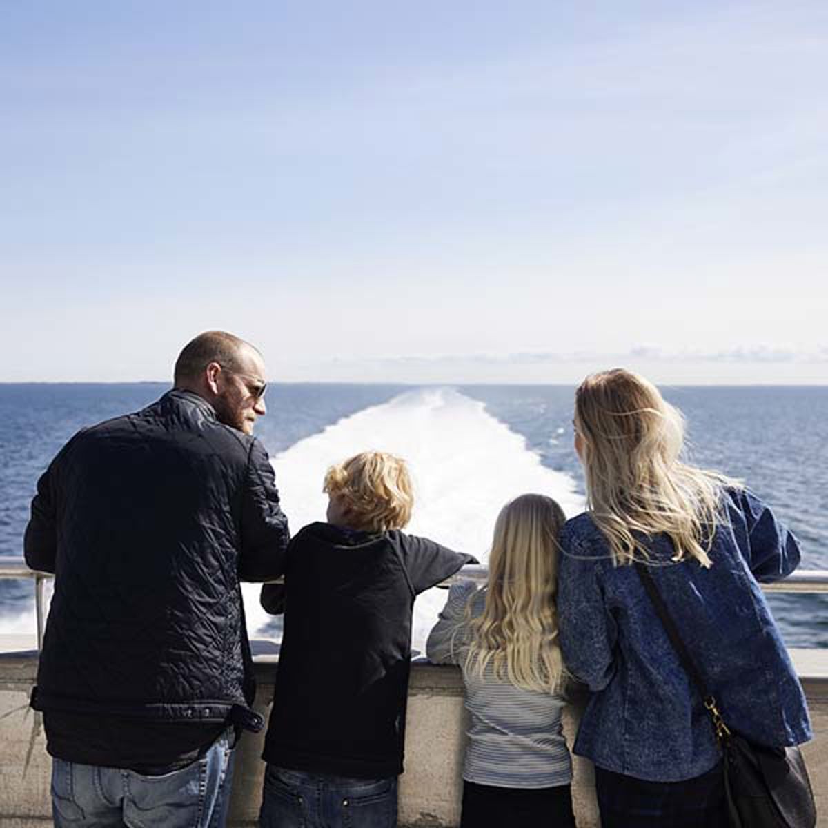 Familie ombord på Molslinjen færge nyder udsigten over bagbord fra dækket i klart solskinsvejr.