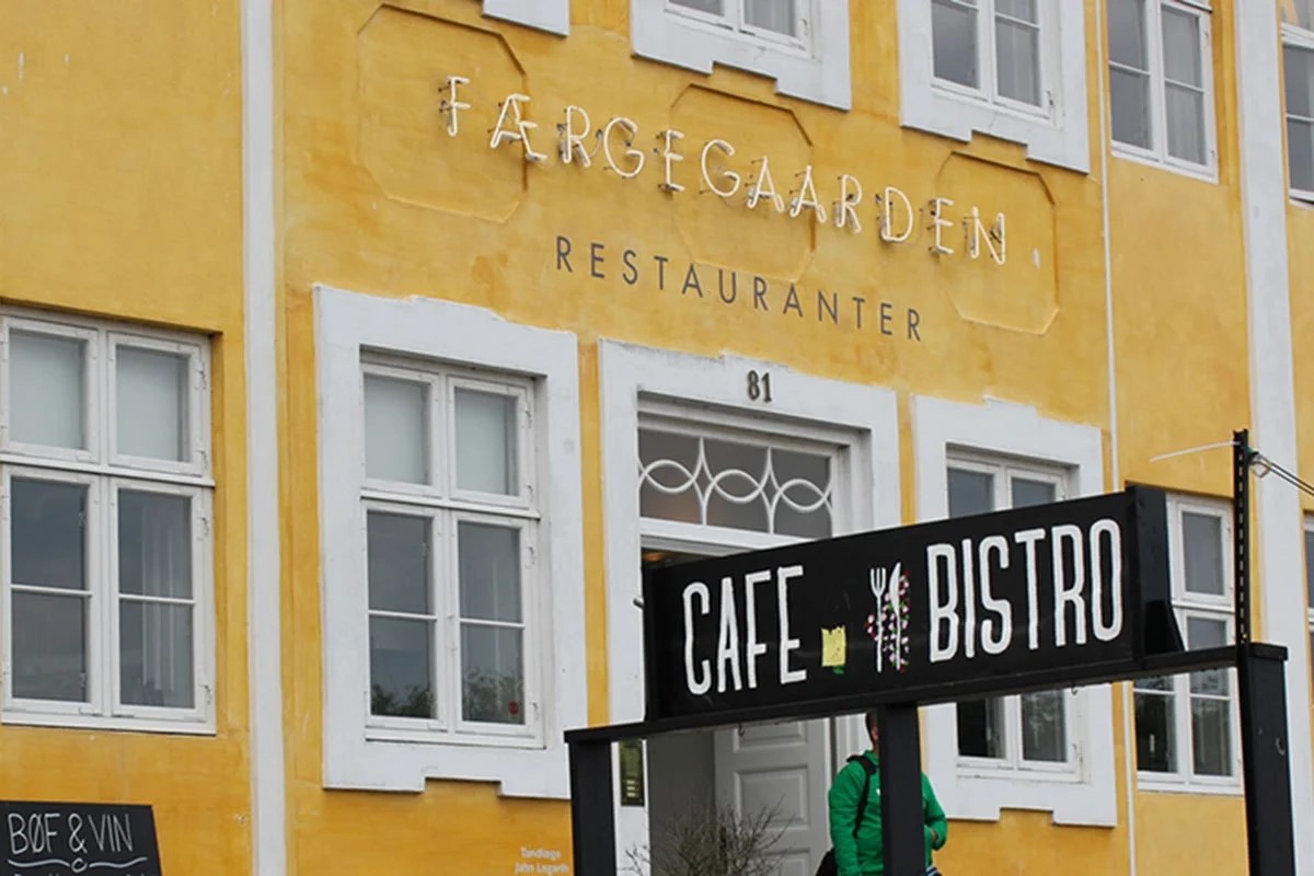 Helsingør bistro med fransk stil mot en solig gul fasad på Færgegaarden restaurang i bakgrunden.