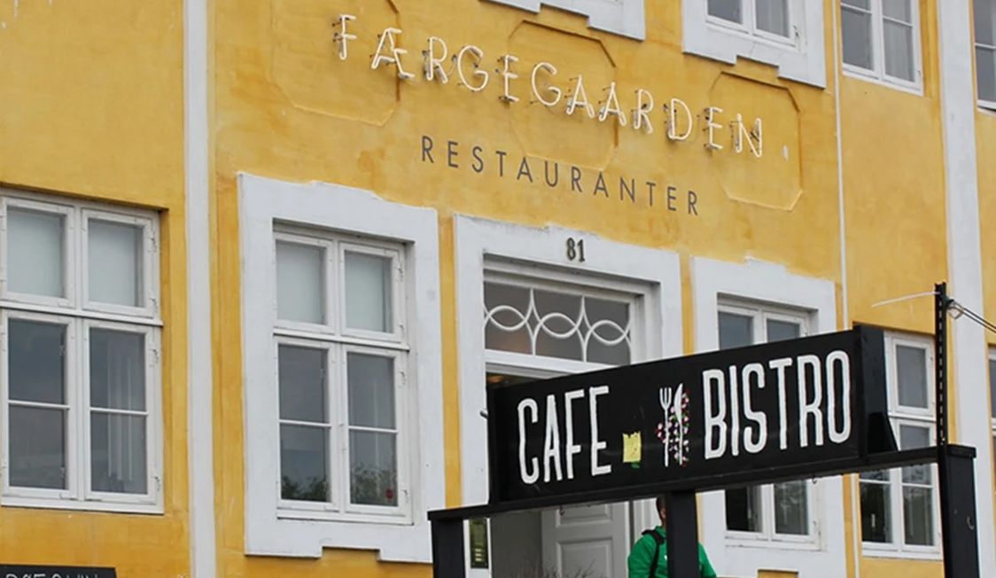 Helsingør bistro med fransk stil mot en solig gul fasad på Færgegaarden restaurang i bakgrunden.