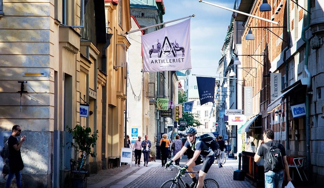 Cyklist kører gennem en livlig, smal gade med folk og butikker i Göteborg centrum, Sverige på en solskinsdag.