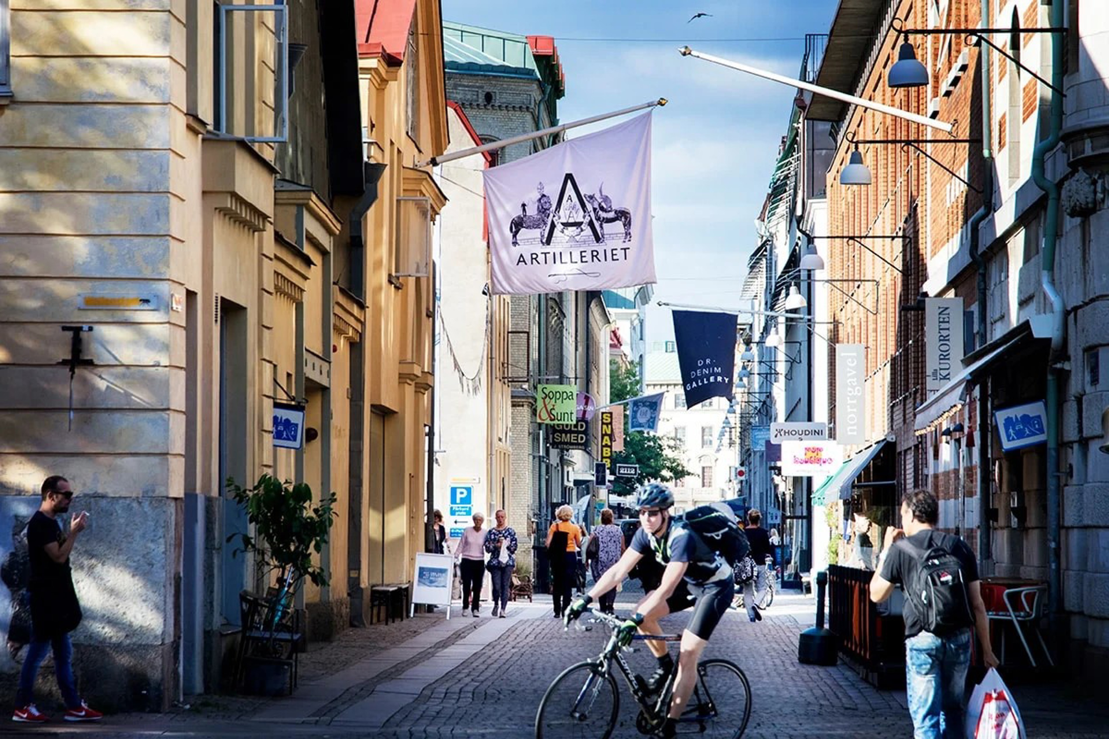 Cyklist i smal, livlig gata med butiker i centrala Göteborg, Sverige, på en solig dag.