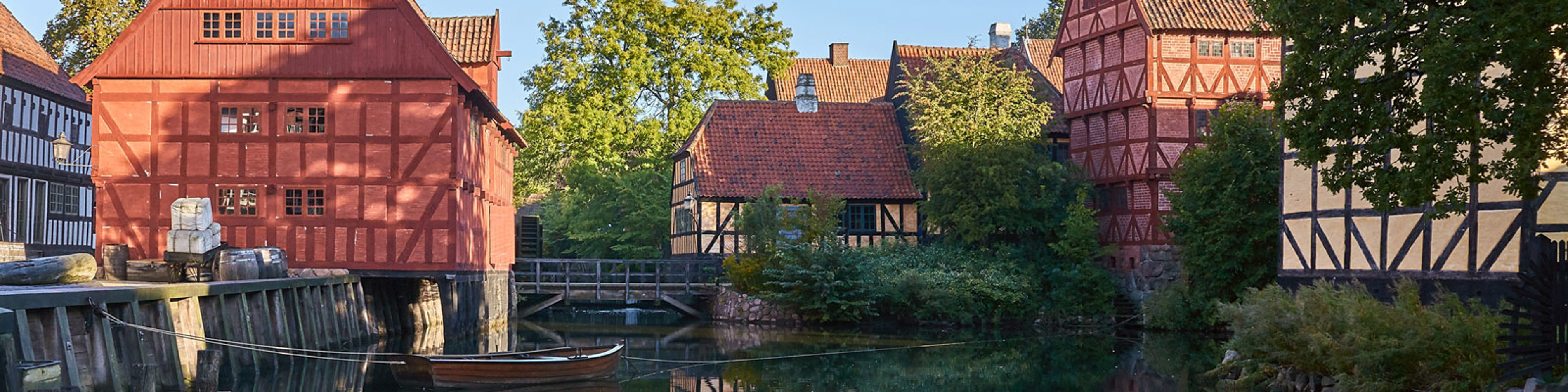 Bindingsværkshuse ved kanalen i Den Gamle By i solrigt vejr, båd fortøjet langs vandkanten.