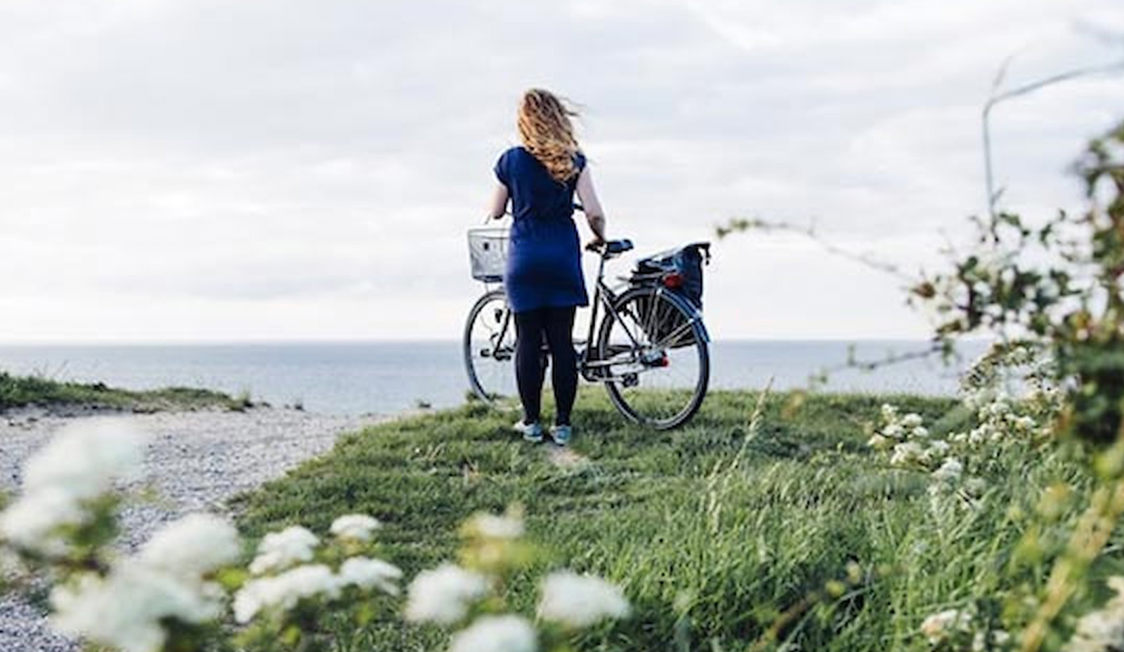 Kvinna med cykel står på klippa vid havet i Nordsjälland, omgiven av grönska och blommor.