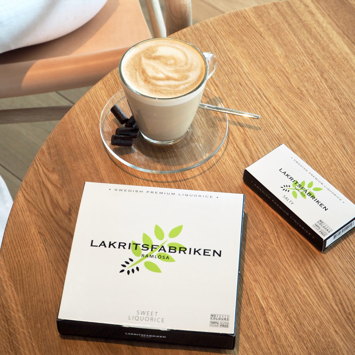Lakritsfabriken lakridsæske og kaffe latte på træbord i caféindstilling.