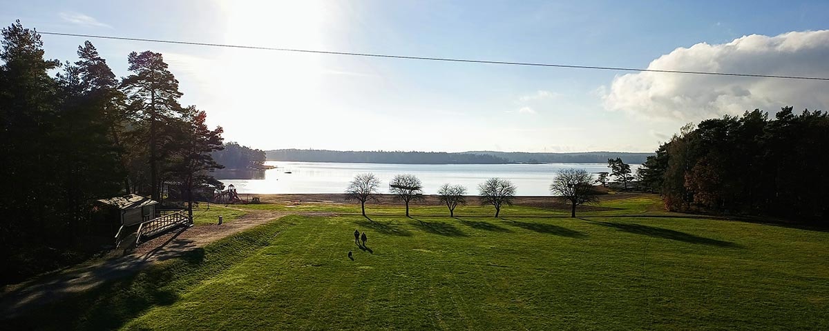 Udigt over græsplæne træer og havet. I distancen ses land på den anden side.