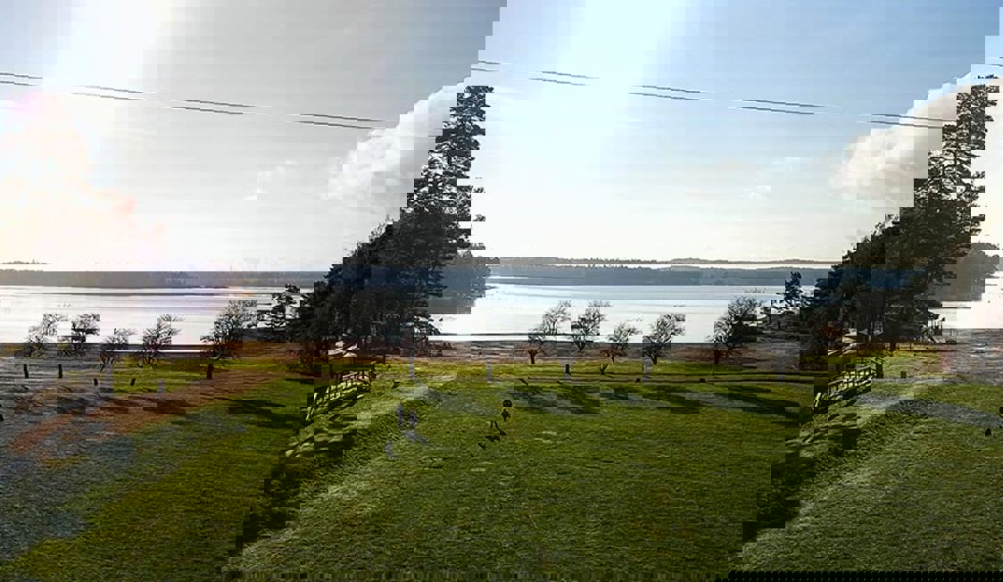 Udigt over græsplæne træer og havet. I distancen ses land på den anden side.