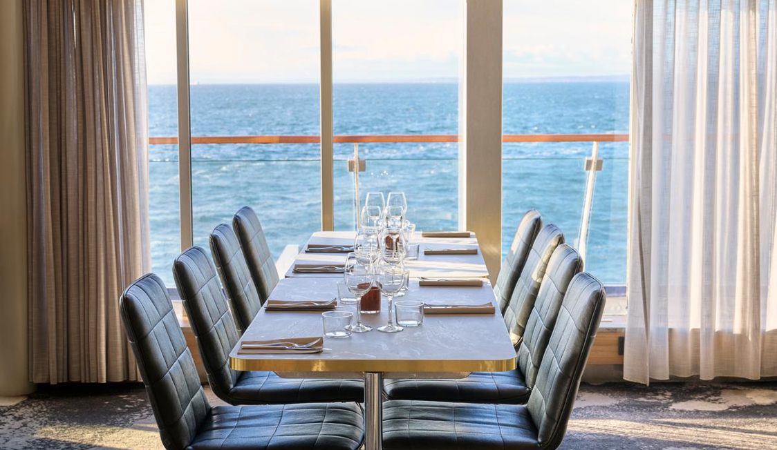 Modern dining table setup with ocean view through large windows, featuring elegant Stemning chairs and tableware.