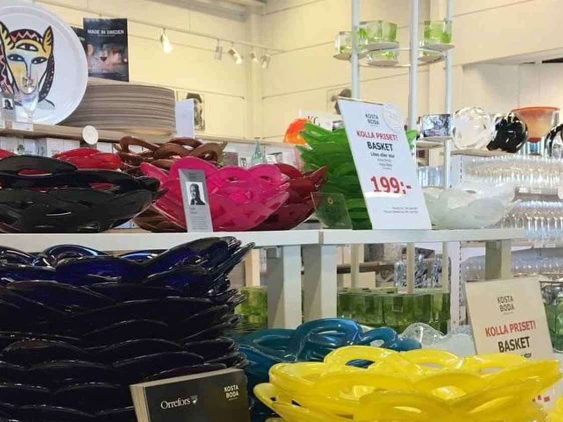 Forskellige farvede Kosta Boda glasfade udstillet på hylder i en butik.