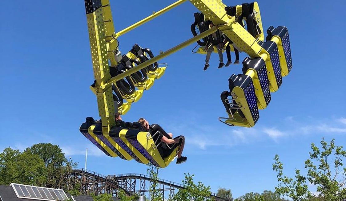 Gul forlystelse i tivoli med passagerer svævende i luften mod klar blå himmel.