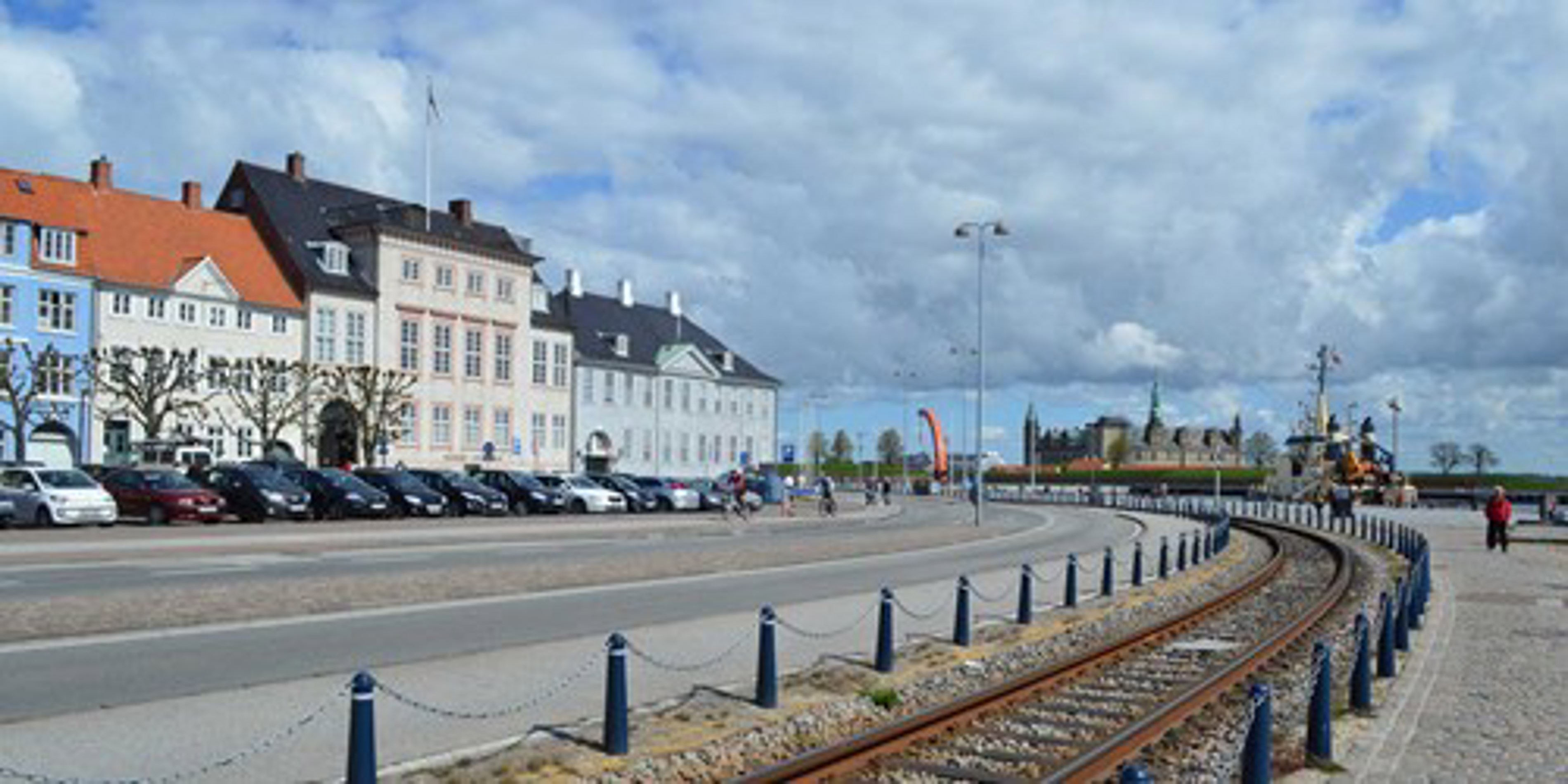 Farverige historiske bygninger langs havnefronten i Helsingør med jernbanespor og blå himmel i baggrunden.