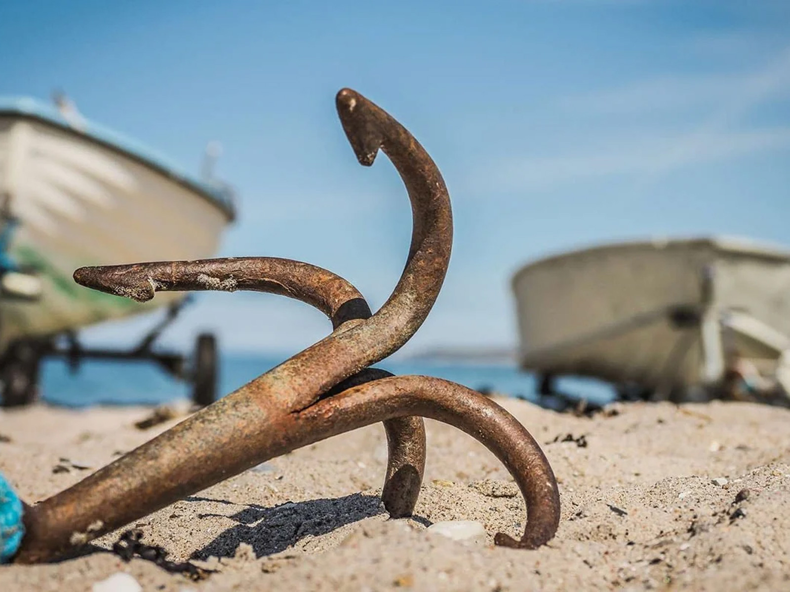 Rostigt ankare på sandstrand med suddiga båtar i bakgrunden i Liseleje, Nordsjälland.