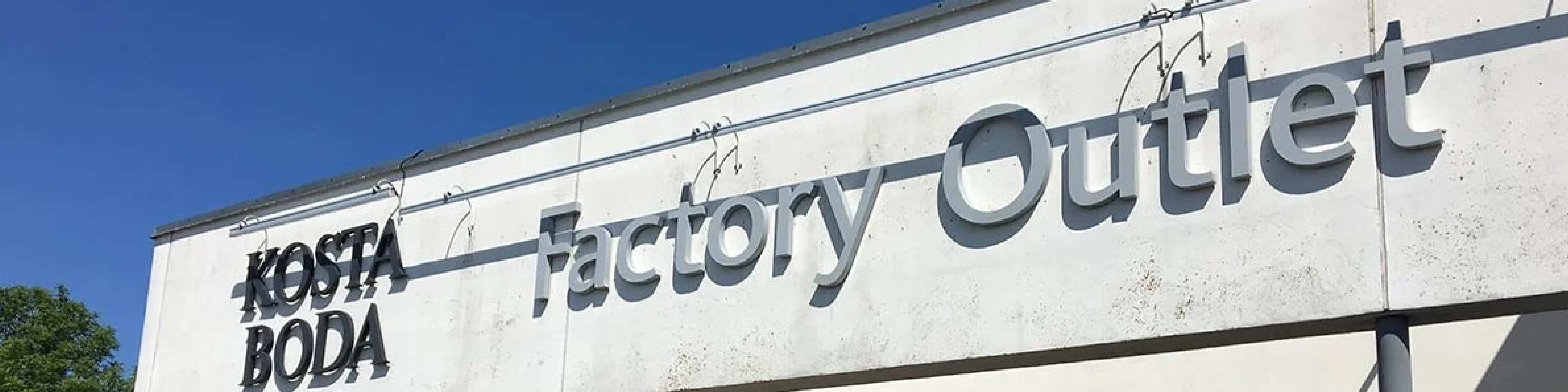 Kosta Boda fabriksudsalg facade i solskin med klar blå himmel i baggrunden.
