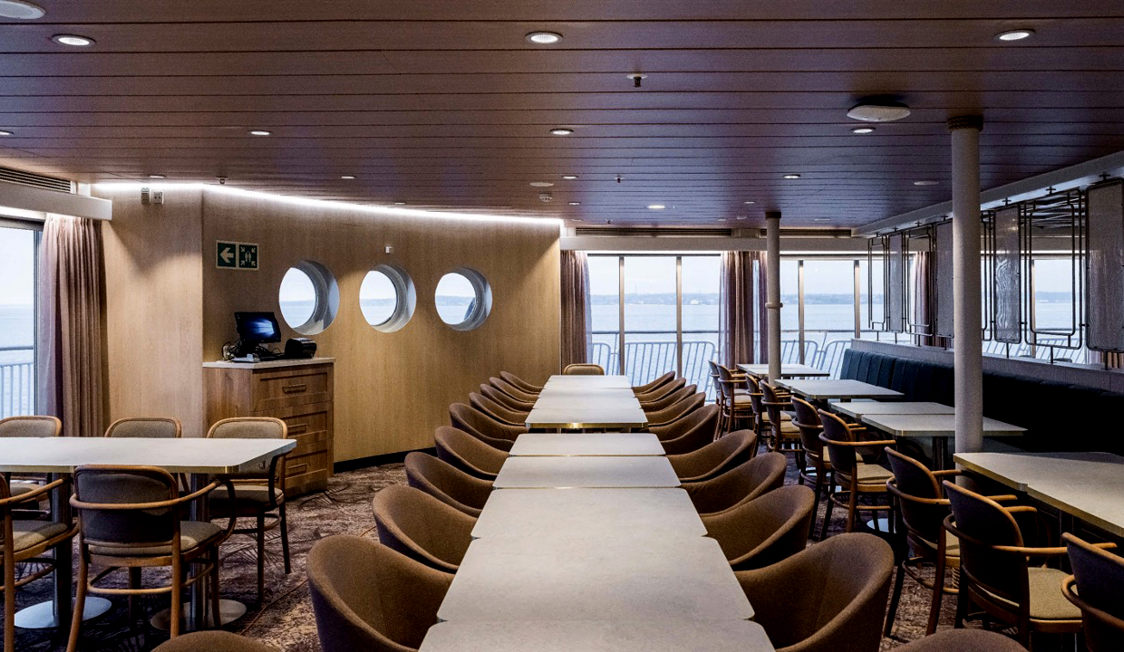 Moderna interiören i färjans matsal med långa bord och bekväma stolar, sedd från fågelperspektiv.