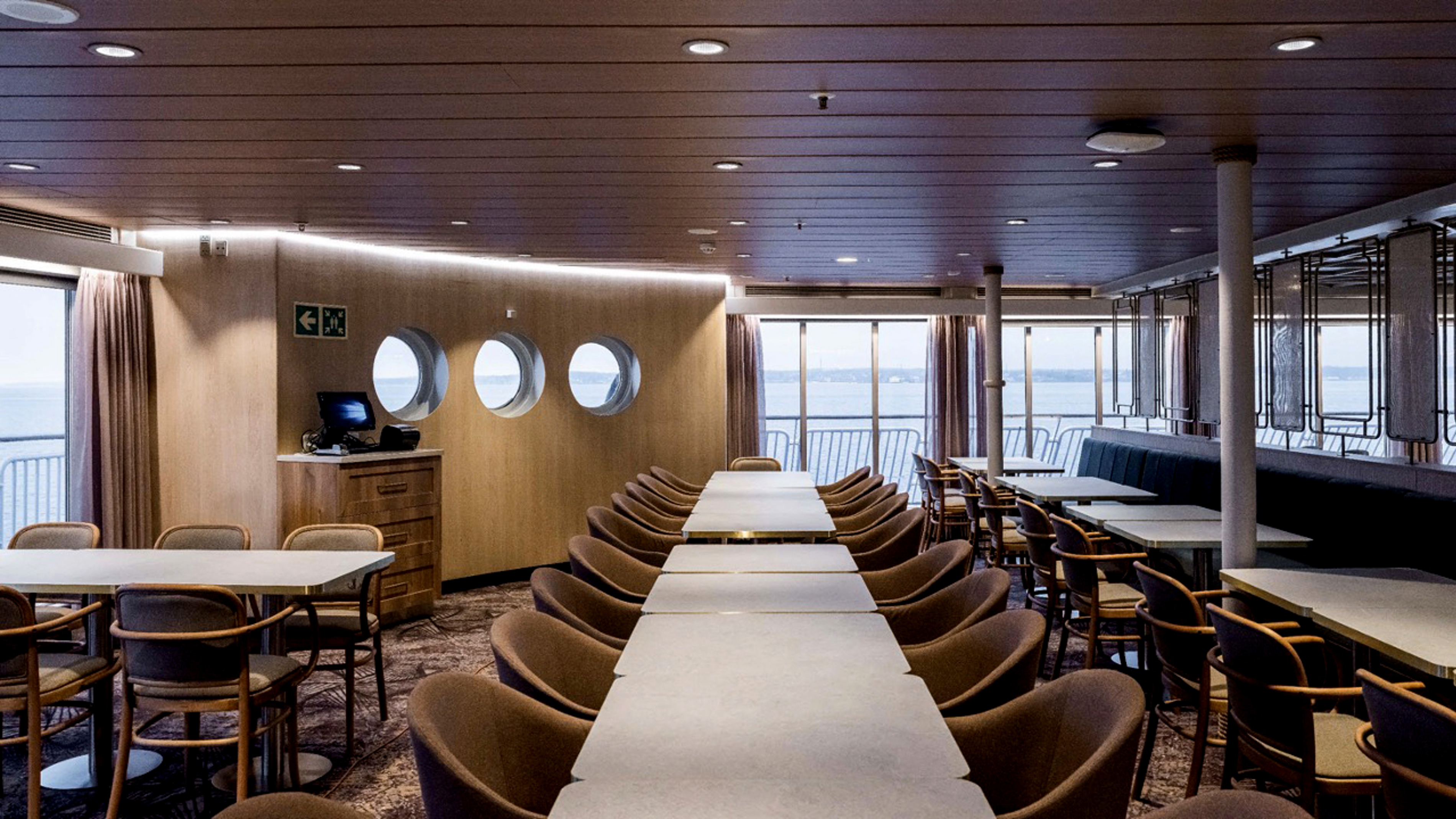 Moderne interiør i færgens spisesal med lange borde og komfortable stole, set i fugleperspektiv.