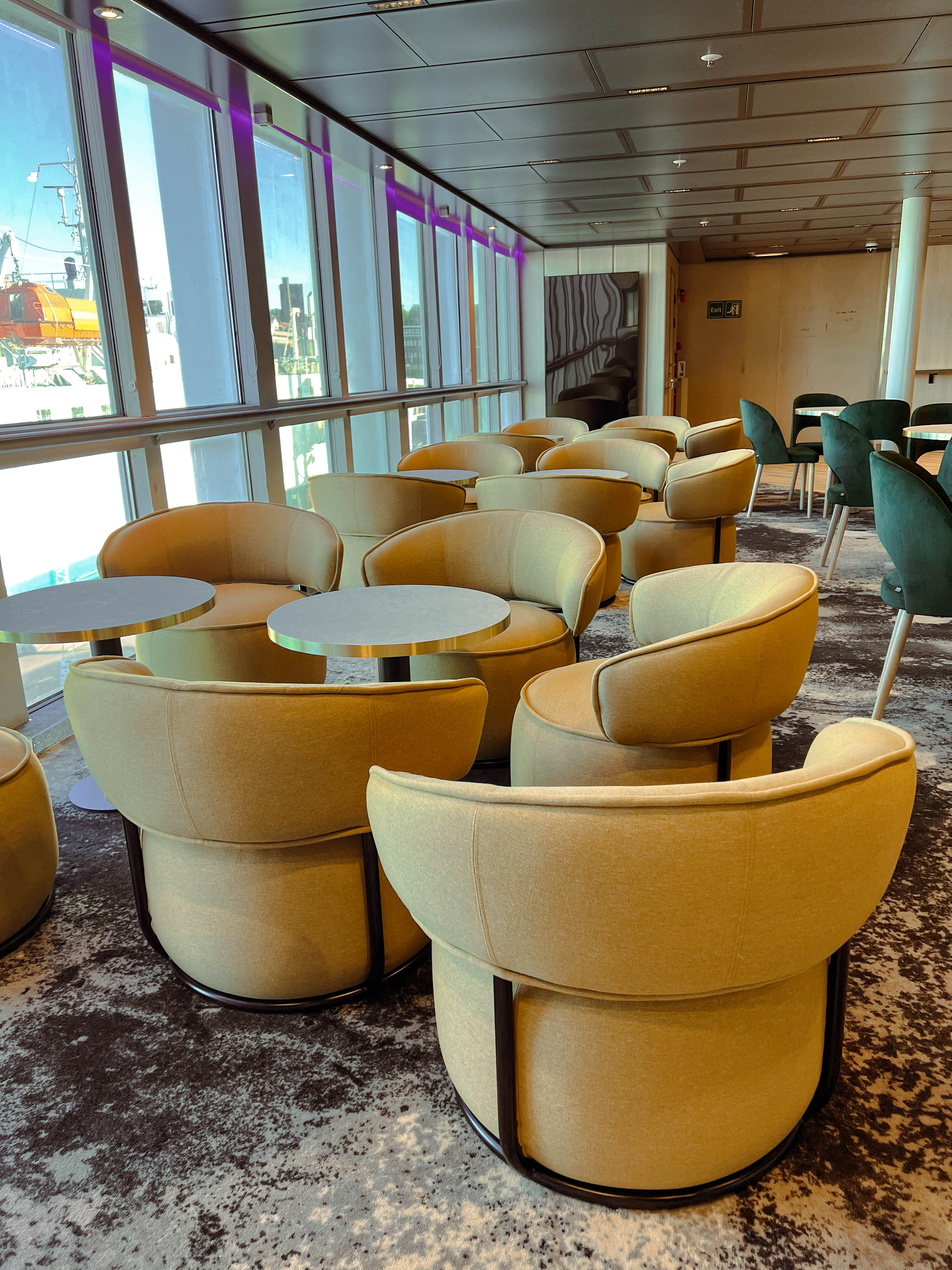 Moderna beige fåtöljer runt bord i hotellounge, bredvid stora fönster som släpper in naturligt ljus.