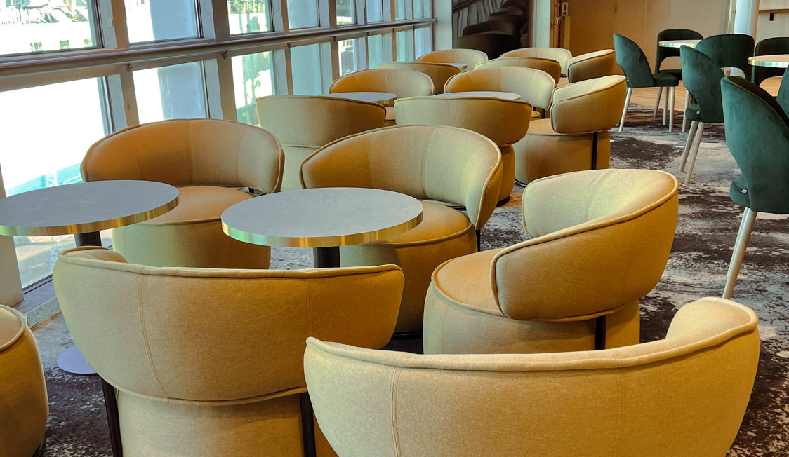 Moderne beige lænestole rundt om borde i hotellets loungeområde ved siden af store vinduer.