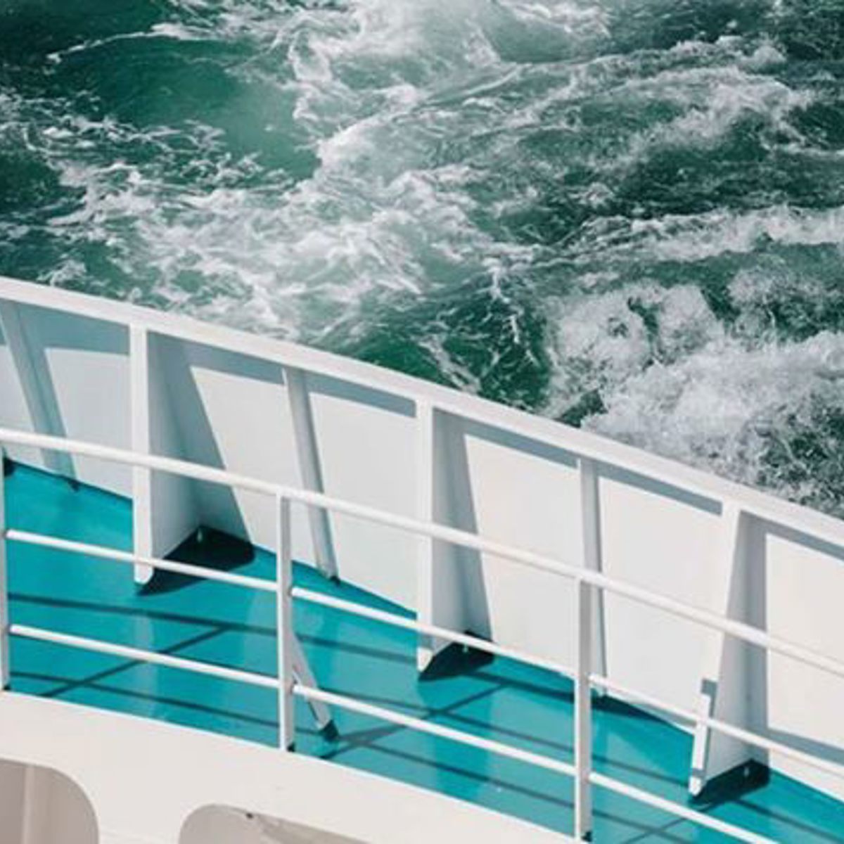 Afsnit af færge sejler gennem åbent, krusende hav med hvide bølger, set fra dækket.