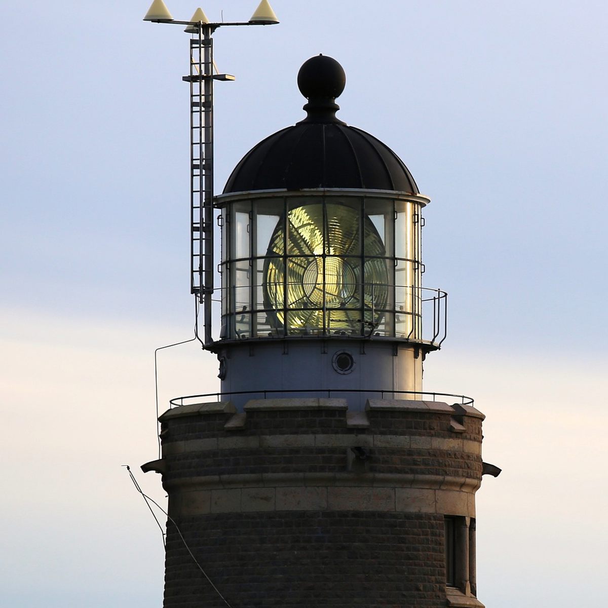 Fyret med glaslanterne står mod en blå himmel ved solnedgang, lyset er tændt og synligt gennem glasset.