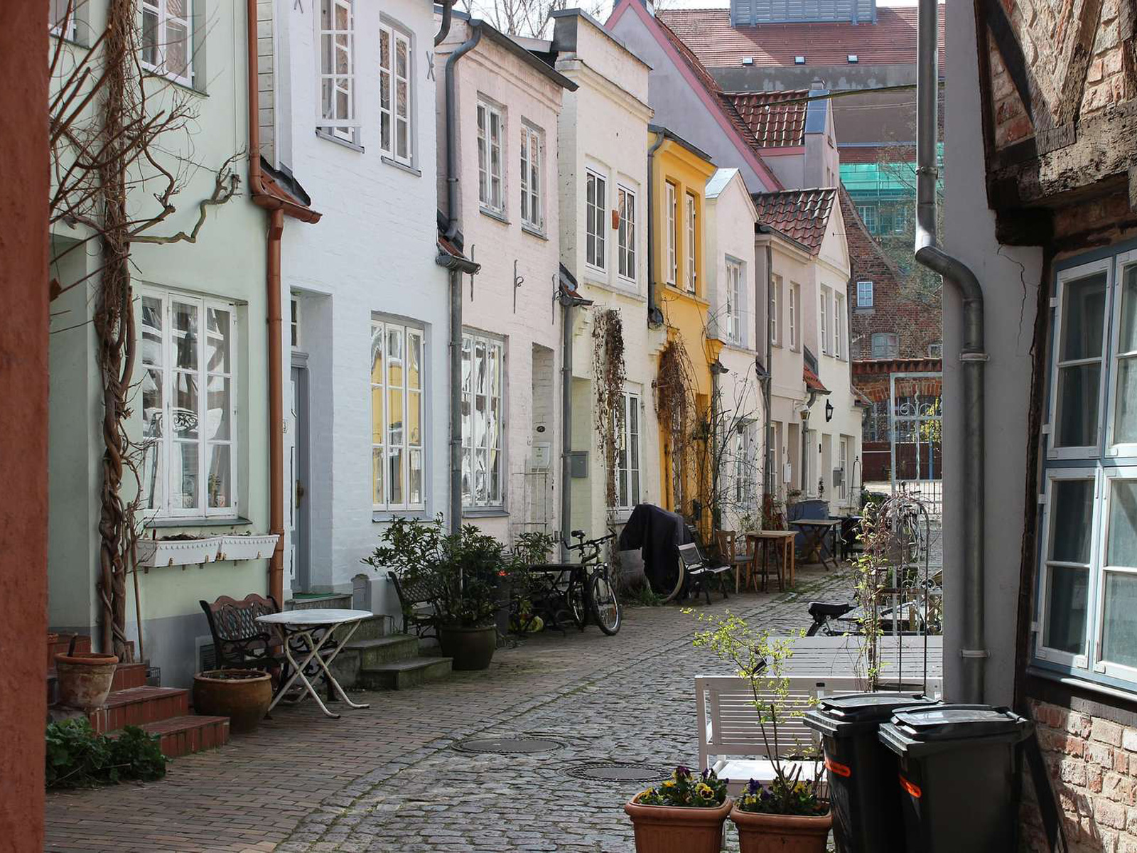 Färgglada radhus med cyklar och utemöbler i en charmig smal gata i Lubeck skapar en pittoresk stadsbild.