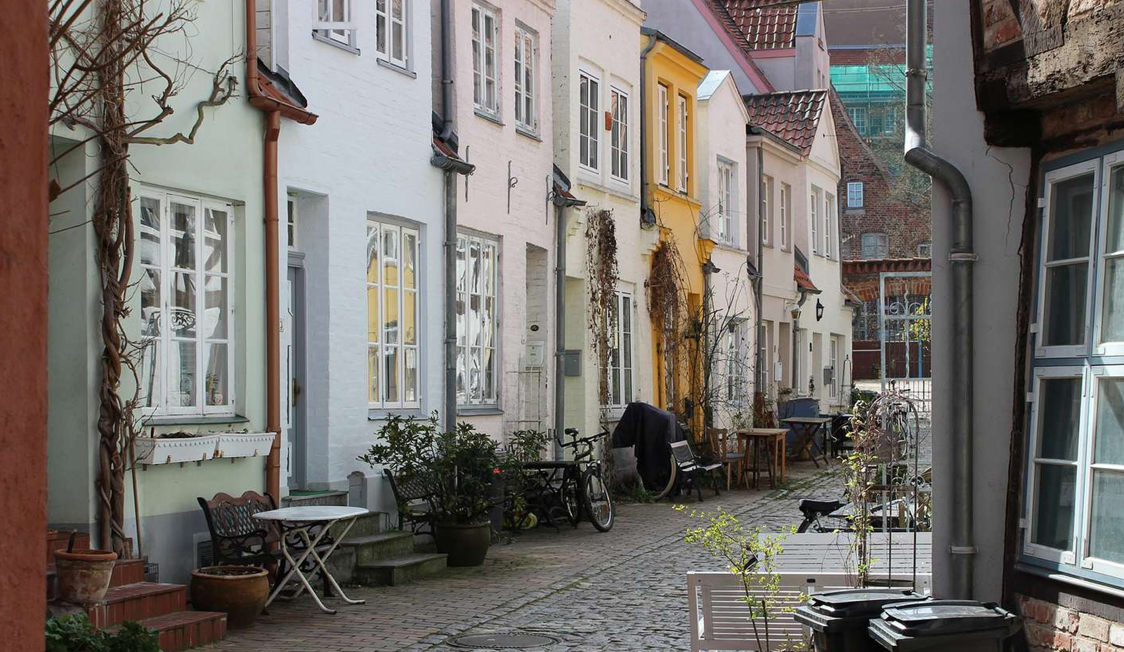 Färgglada radhus med cyklar och utemöbler i en charmig smal gata i Lubeck skapar en pittoresk stadsbild.