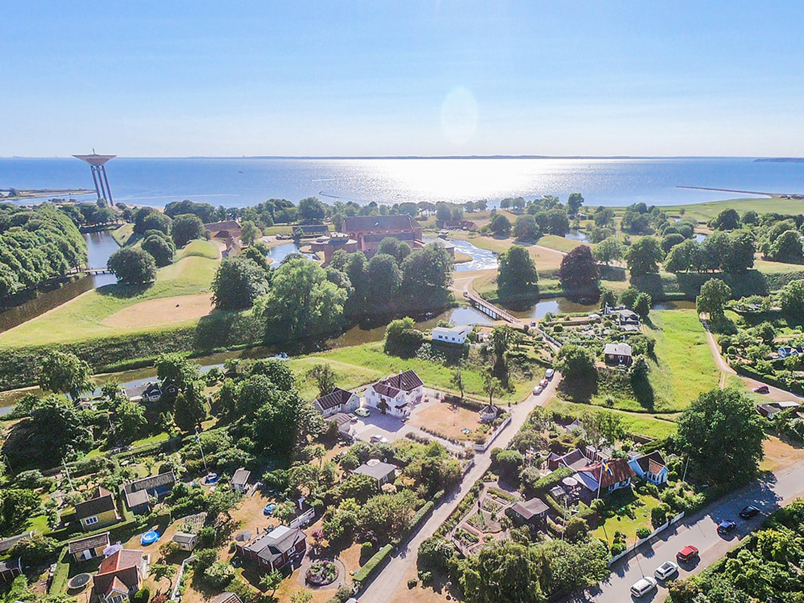 Luftfoto af landskab med grønne områder, huse og udsigt til havet ved Kalundborg på en solskinsdag.