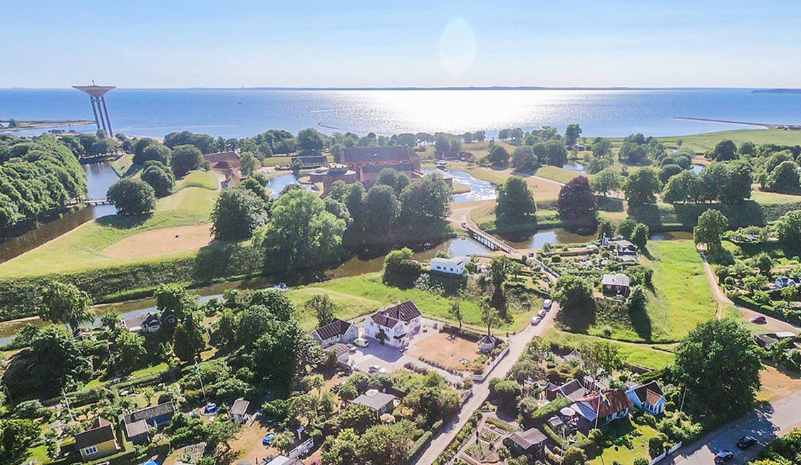 Luftfoto af landskab med grønne områder, huse og udsigt til havet ved Kalundborg på en solskinsdag.