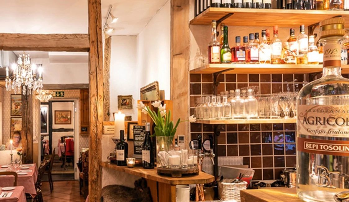 Barinteriør med træhylder fyldt med vinflasker og glas, hyggelig stemning og dæmpet belysning i en restaurant.