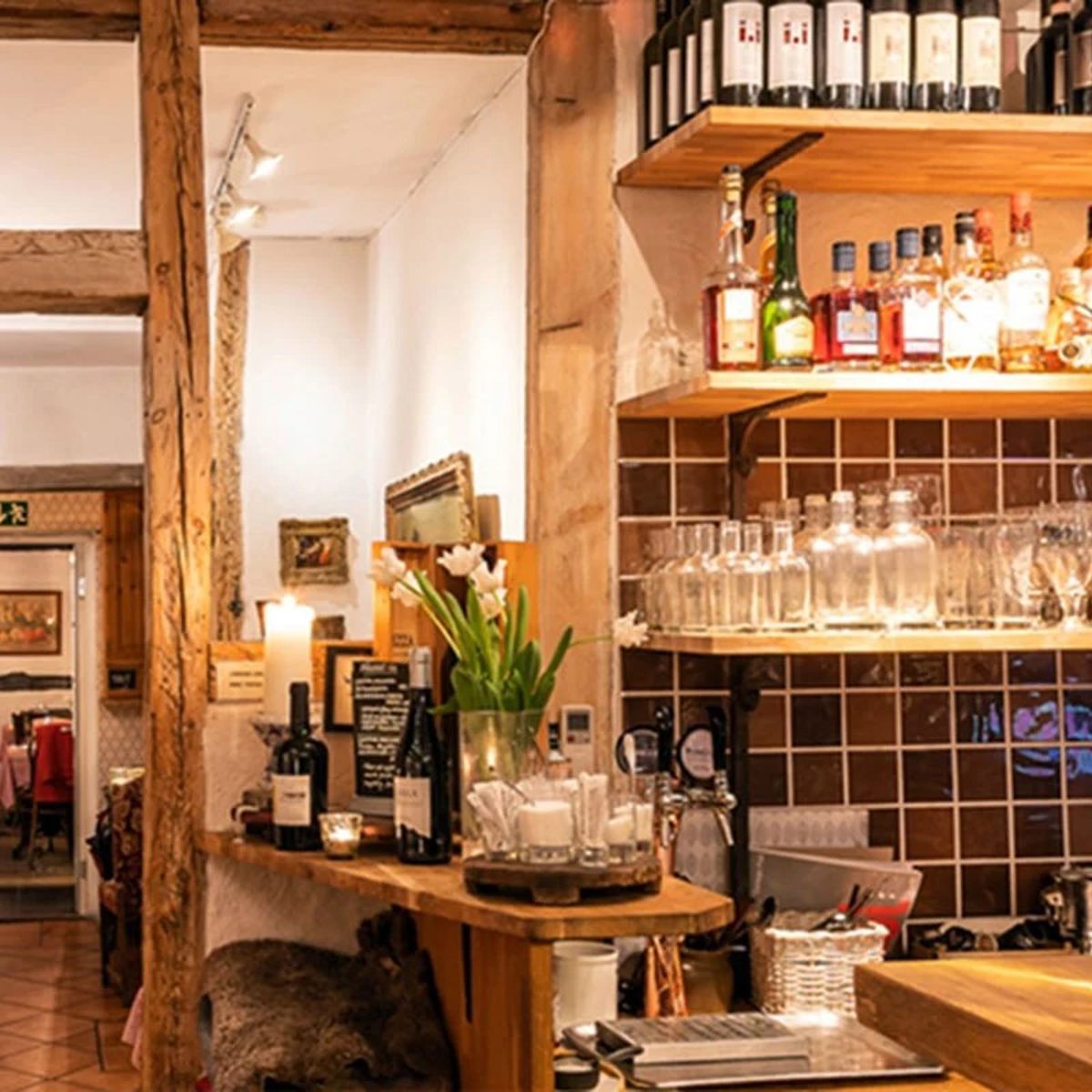 Barinteriør med træhylder fyldt med vinflasker og glas, hyggelig stemning og dæmpet belysning i en restaurant.