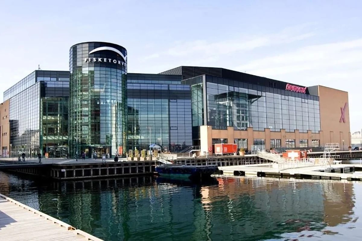 Fisketorvet köpcentrum med glasfasad vid vattnet, sedd från kajen en solig dag.