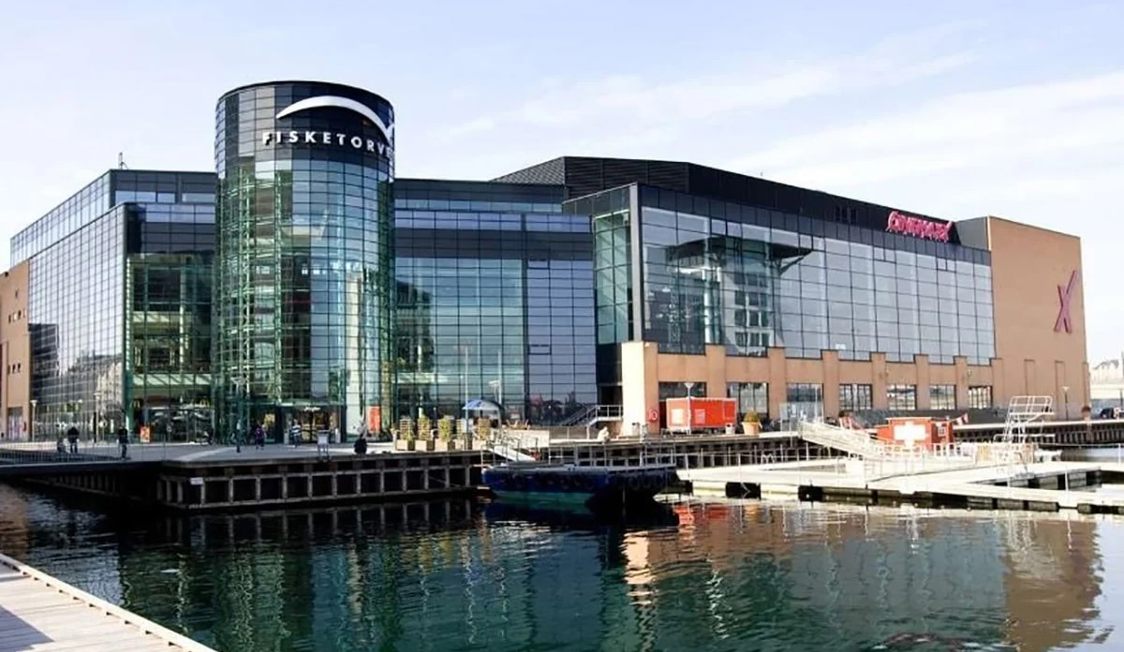 Fisketorvet köpcentrum med glasfasad vid vattnet, sedd från kajen en solig dag.