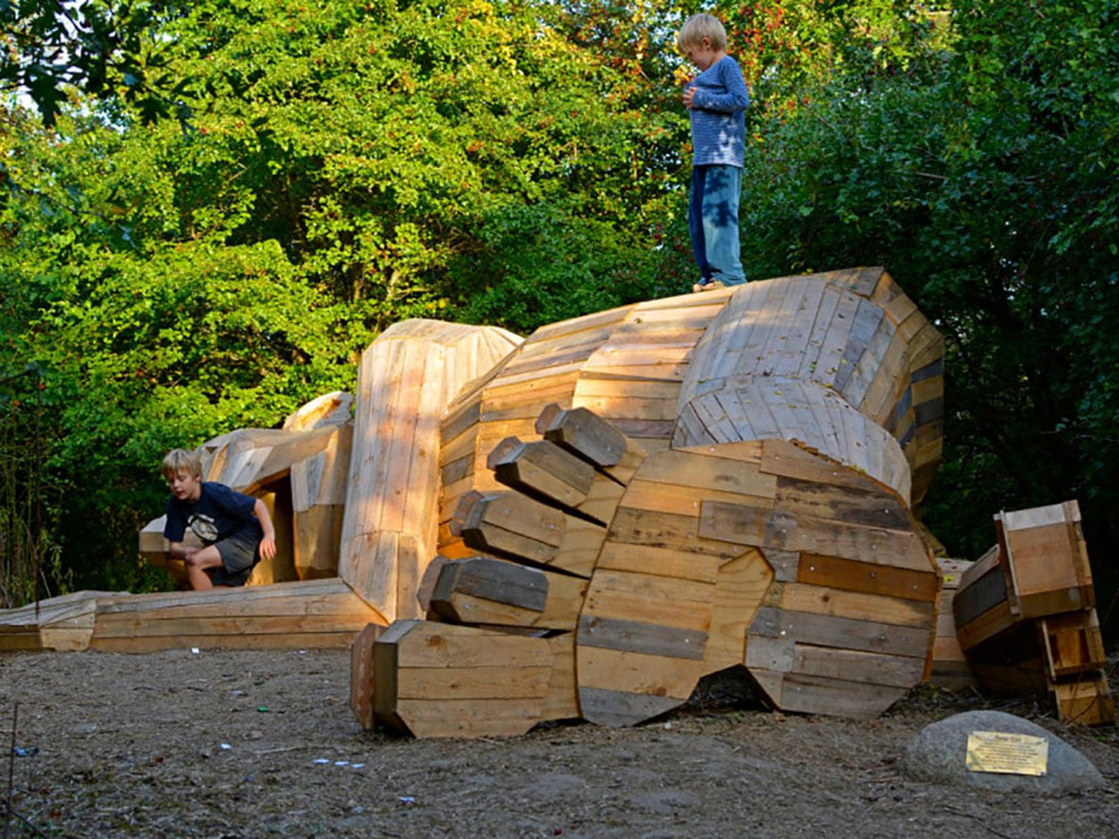 Stort trätroll från Kph Jättetrollen i en skogsmiljö, barn leker runt den konstnärliga skapelsen.