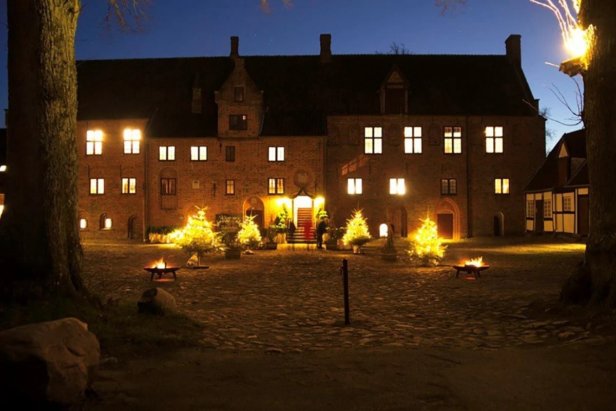 Esrum Kloster i kvällsljus med lysande dekorationer och eldar på gårdsplanen framför den historiska byggnaden.