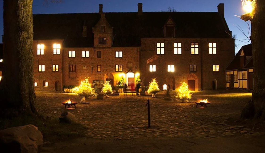 Esrum Kloster i kvällsljus med lysande dekorationer och eldar på gårdsplanen framför den historiska byggnaden.