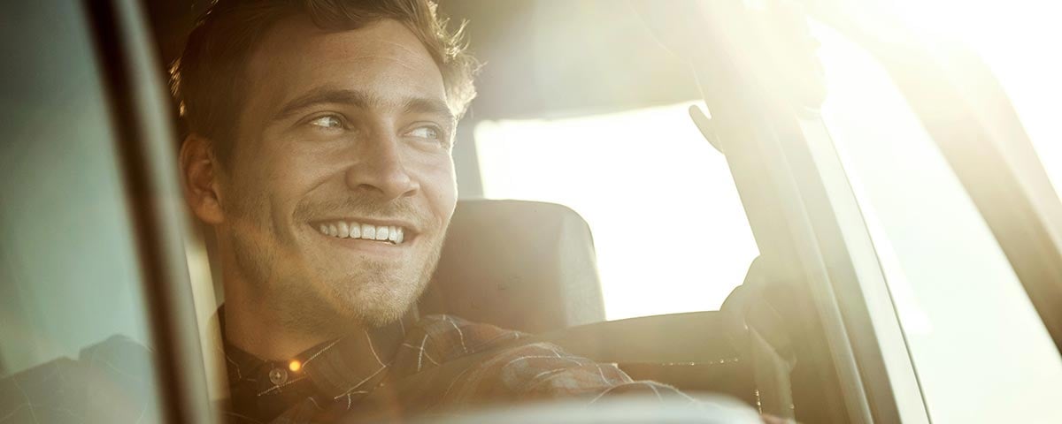 En mand sidder i en bil og smile mens solen skinner ind gennem bagruden.